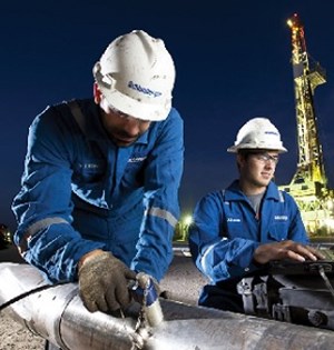 Two SLB workers in front of a drilling rig