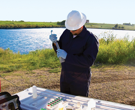 A Baker Hughes field chemist draws a sample from a pond for pretreatment water analysis.