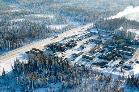 Aerial view of an Apache pad site in the Horn River Basin in midwinter. The manifold is under the hoarding to the right of the yellow frac tree shelters.
